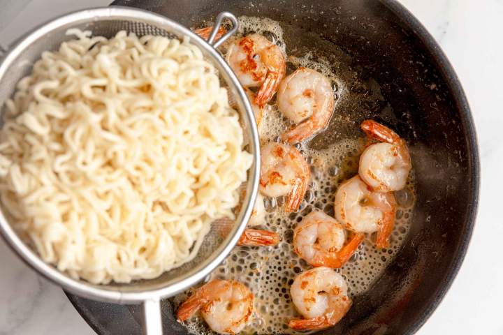 Adding noodles to the shrimp for Ginger Scallion Noodles with Shrimp