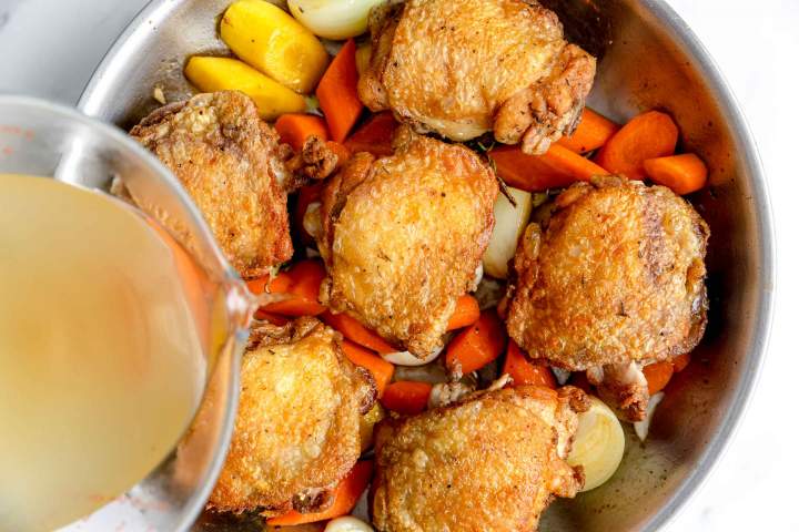 Adding chicken stock to chicken and vegetables for Oven-Baked Chicken Thighs with Carrots