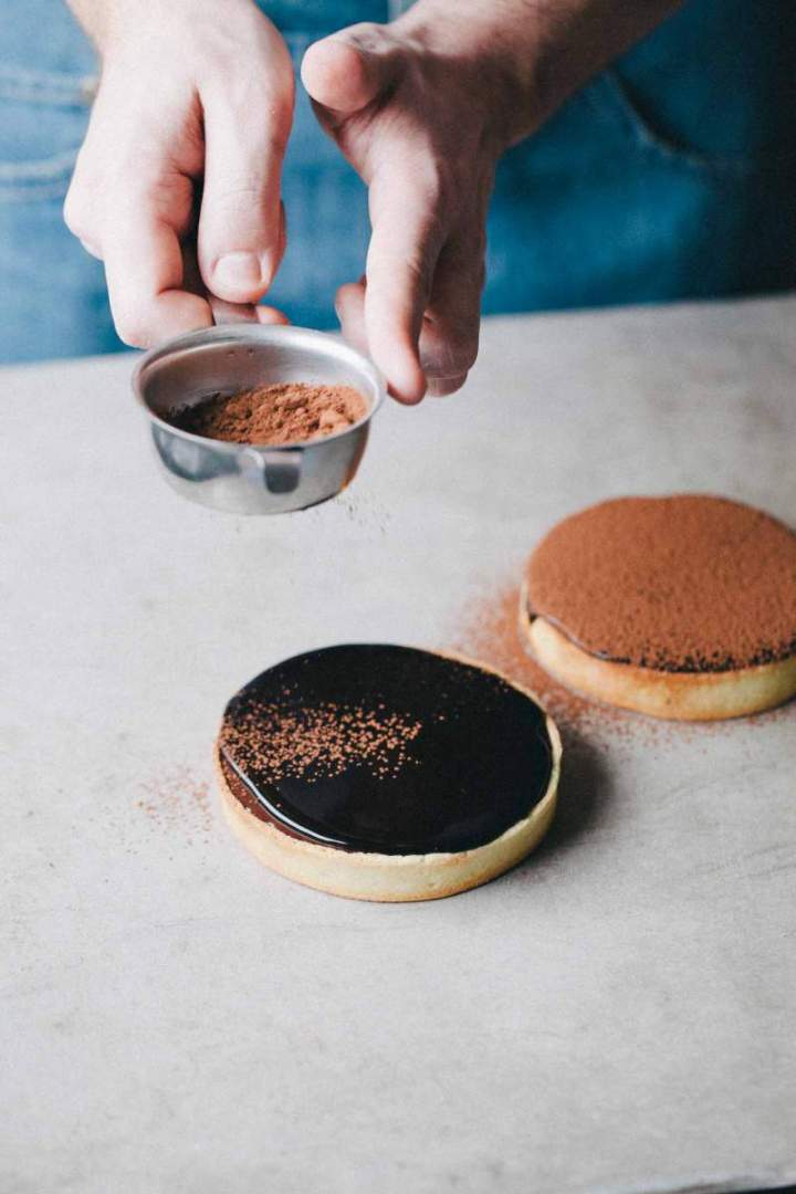Dusting cacao over baked chocolate tarts with cacao glaze