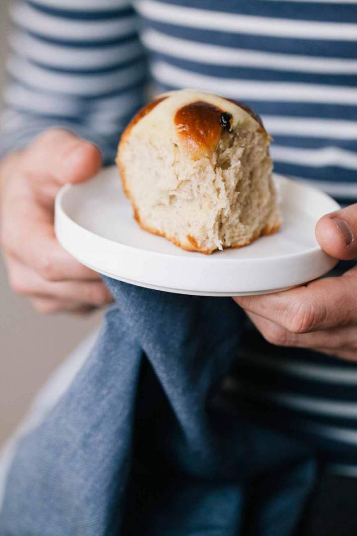 One Baked hot cross buns served on a plate, held in hand